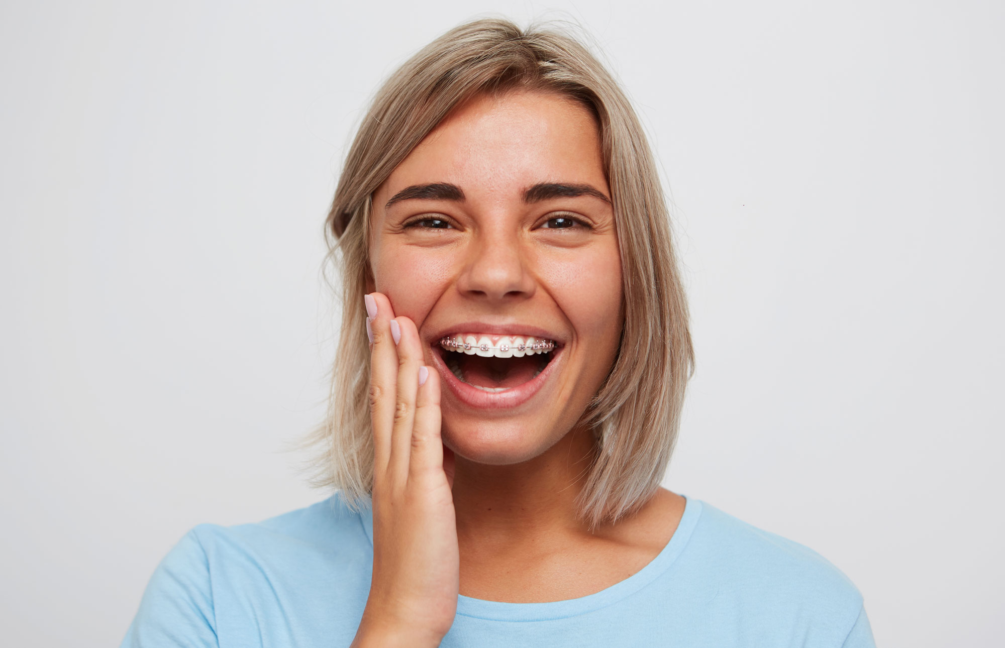 Young woman wearing braces smiling with hand to face against white background