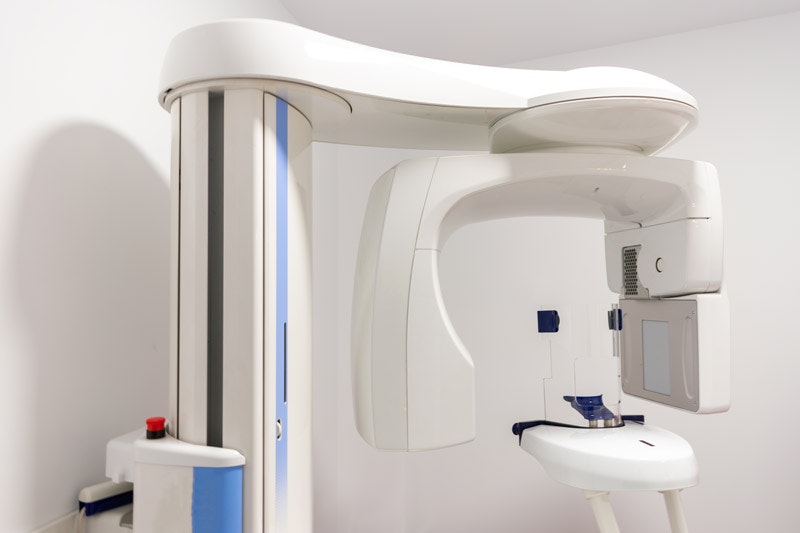 Modern dental panoramic X-ray machine in bright clinical treatment room.