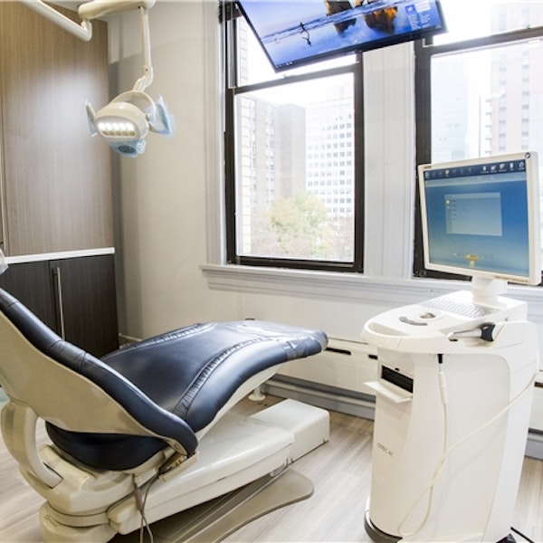 Modern dental operatory with blue chair, overhead light, computer monitors, and city skyline view through windows.