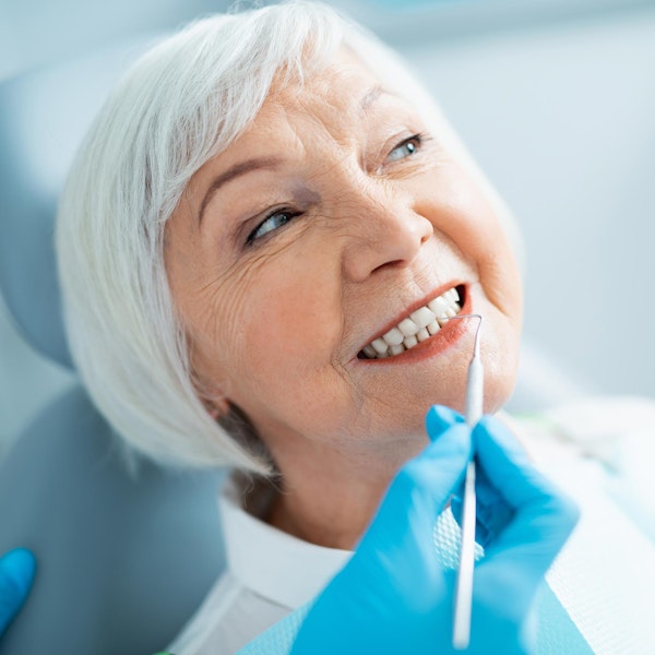 Senior woman smiling during dental examination with dentist wearing blue gloves.