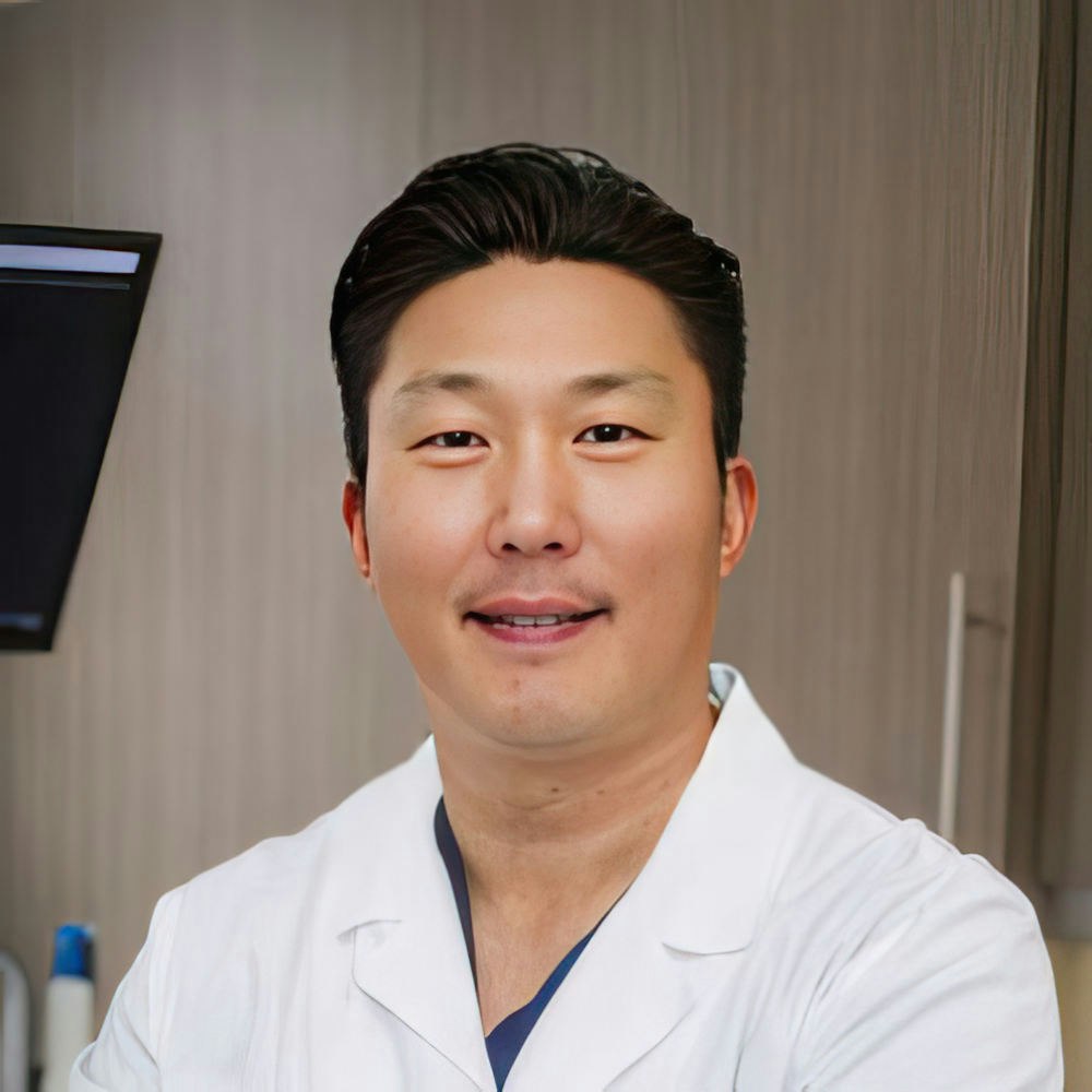 Professional male dentist in white coat smiling at camera in modern dental office setting.