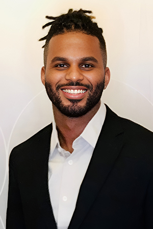 Professional headshot of smiling man in black blazer and white shirt against neutral background.