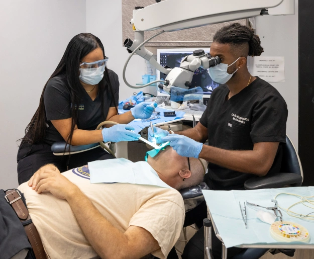 Two dental professionals in masks perform oral examination on patient in clinical setting.